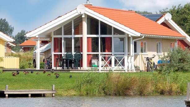 Una casa con techo rojo, ventanas grandes y un muelle que se adentra en el agua.