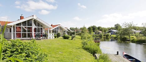 A lakeside property with a grassy area, a dock, and a row of houses with large windows.