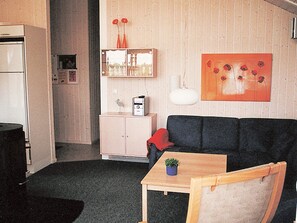 A room with a black sofa, a wooden table with a plant, a white cabinet, and a painting on the wall. - Holiday Home in Otterndorf (Otterndorf)