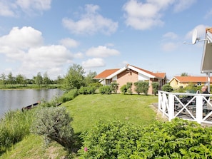 Een huis met een rood dak, een witte omheining en een waterpartij op de achtergrond.