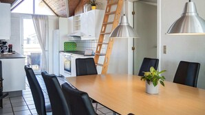 A modern kitchen with a wooden ceiling, a dining table with chairs, and a staircase leading to an upper level.