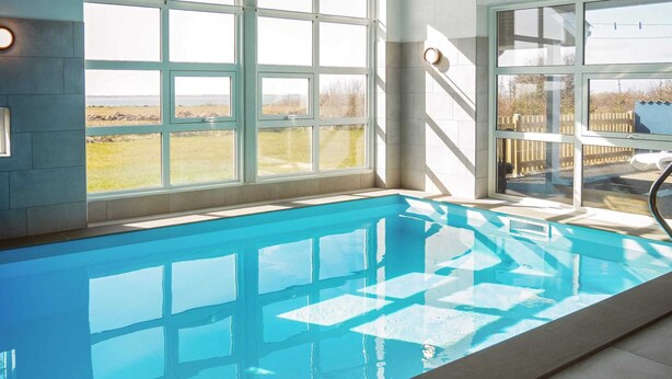 An indoor swimming pool with clear views of the outdoors through large windows.