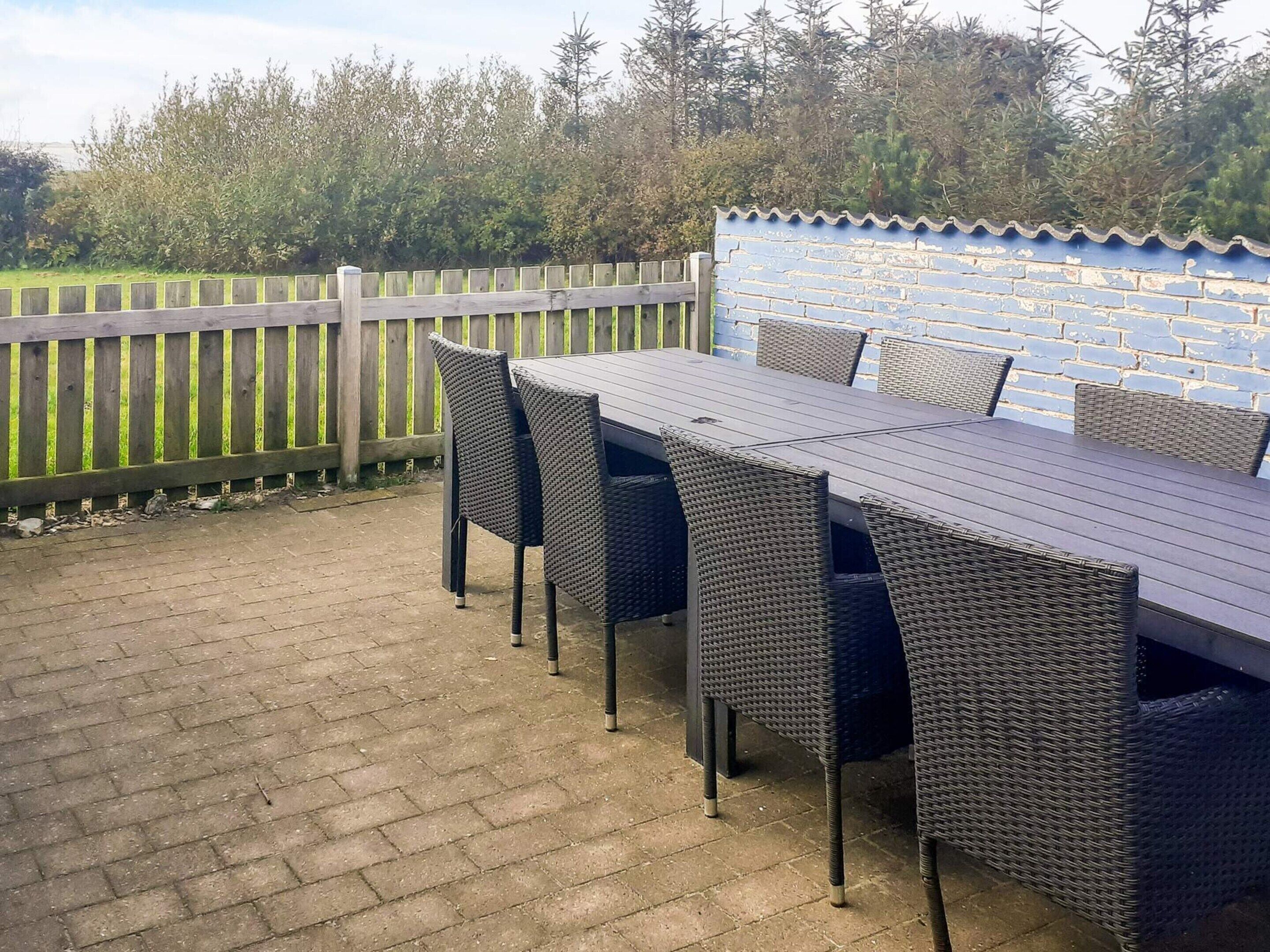 Una terrazza esterna con tavolo e sedie, pavimento in mattoni, recinzione in legno e parete azzurra con tetto in tegole.
