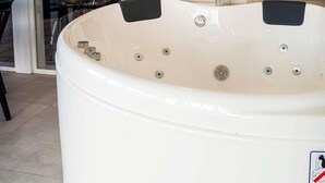 A large white hot tub with multiple jets, a black control panel, and a safety sign.