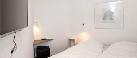 Une chambre à coucher avec un lit, des tables de chevet, un téléviseur fixé au mur et un tableau encadré.