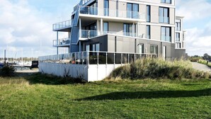A multi-story residential building with balconies, large windows, and a grassy foreground.