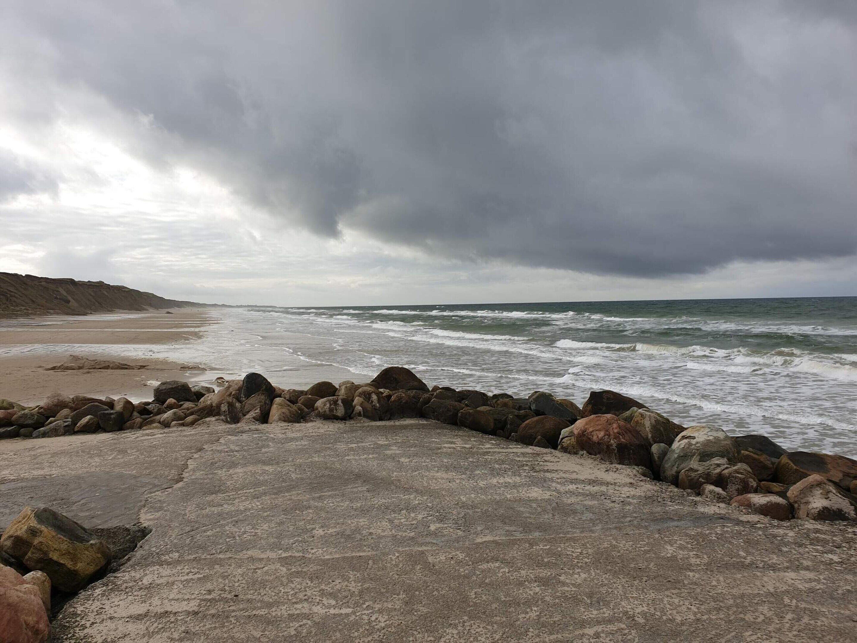 Una playa con costa rocosa y olas rompiendo sobre la arena.
