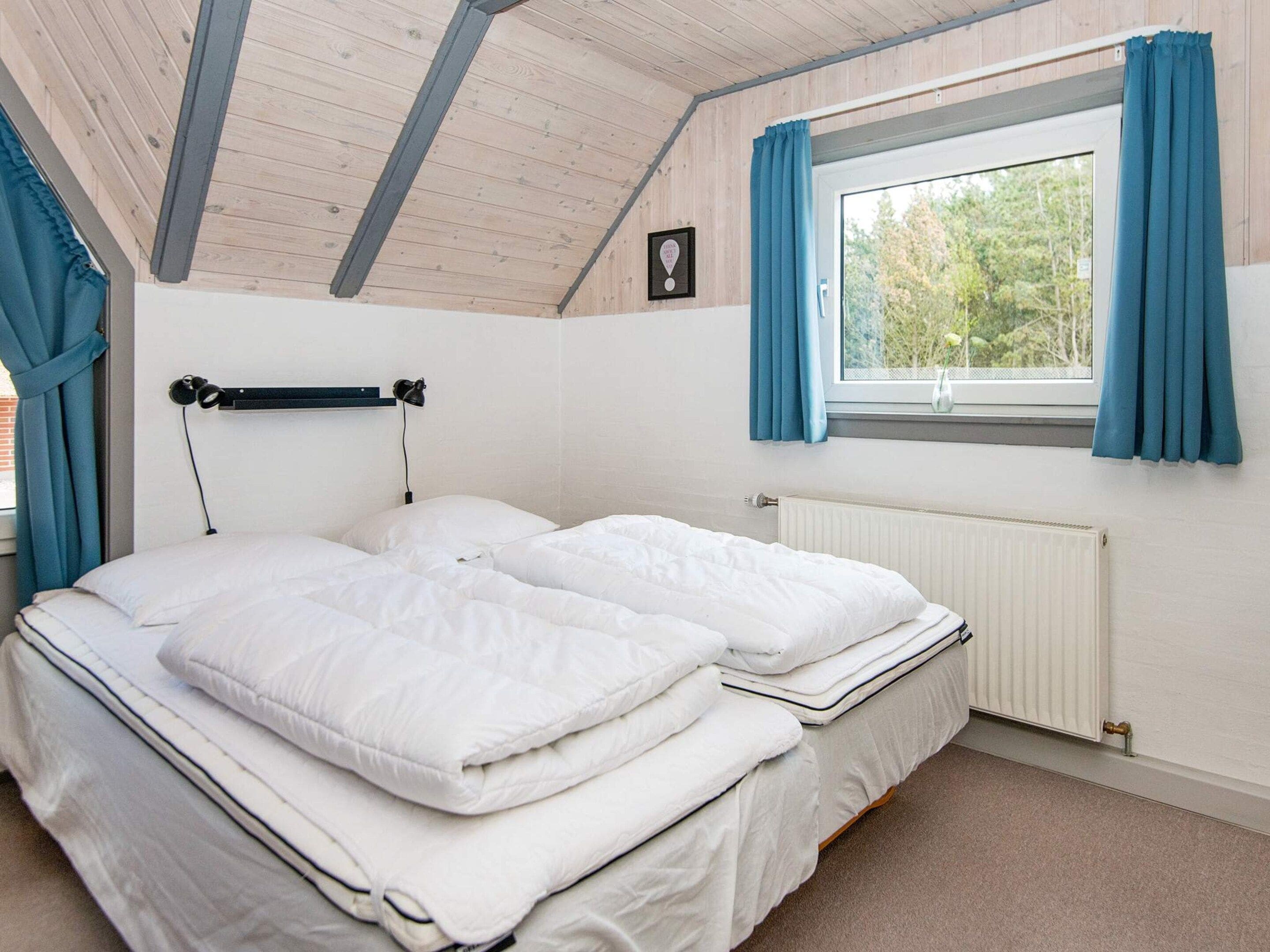 A bedroom with a bed, a window with curtains, a radiator, and a wooden ceiling.