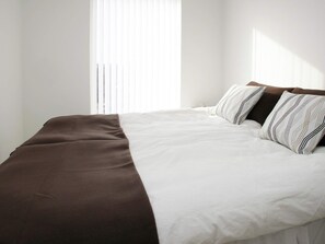 A neatly made bed with a brown and white bedspread, white pillows, and a window with blinds in the background.