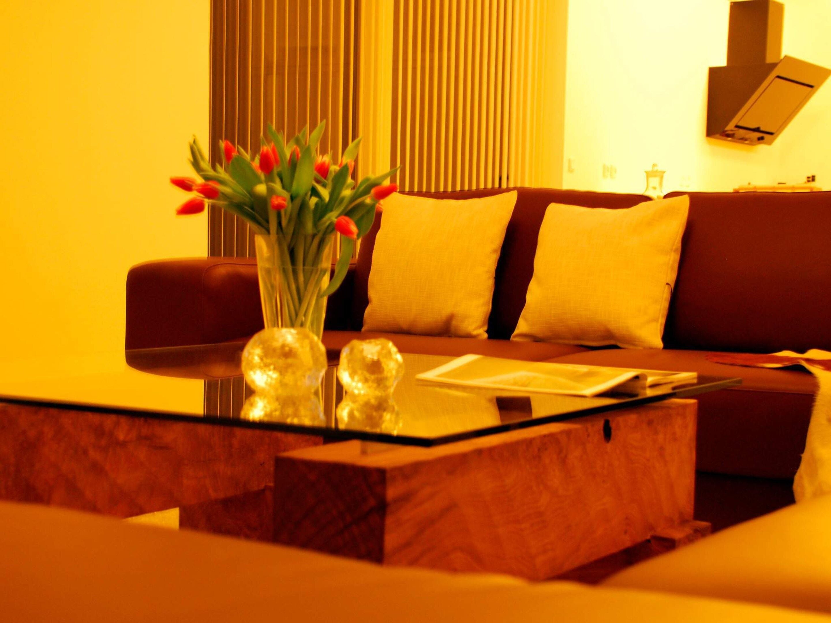 En moderne stue med en sofa, et sofabord i glas og en vase med røde blomster.