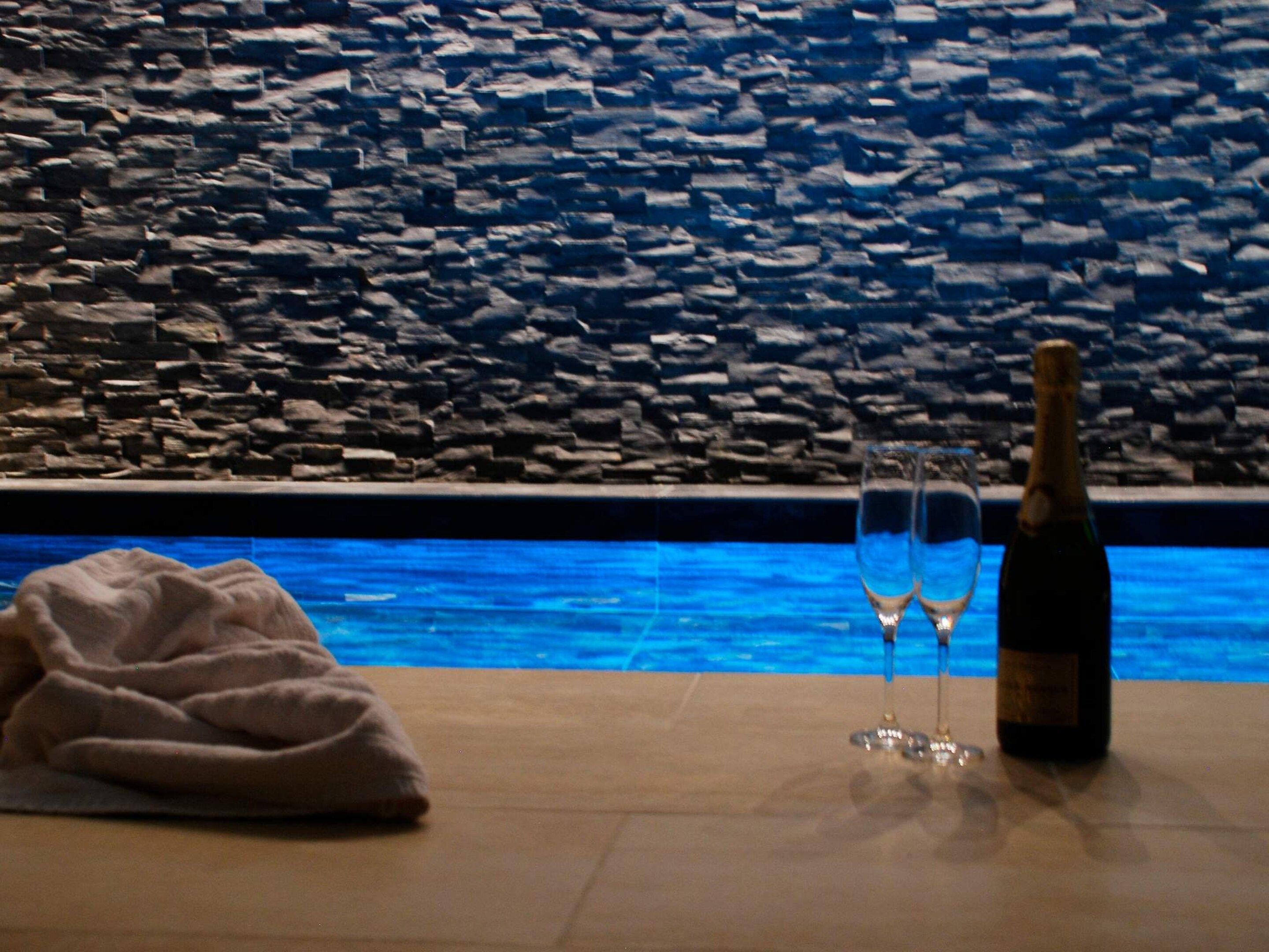 En stenvæg, en pool, en champagneflaske og to glas på et bord.