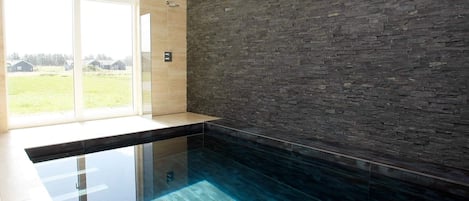 A modern bathroom with a glass-enclosed shower, a stone wall, and a view of the outdoors.
