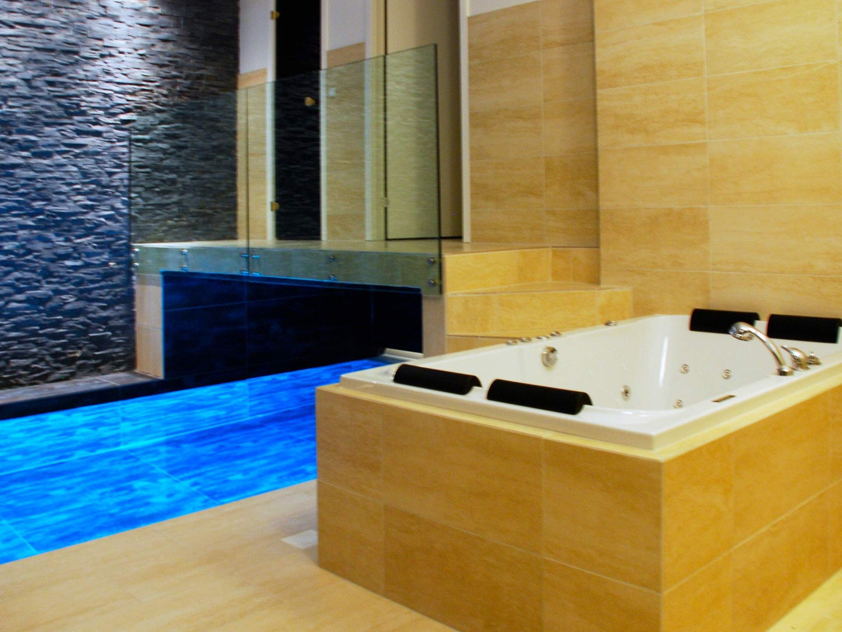 A modern bathroom with a large bathtub, a glass-enclosed shower, and a stone wall.