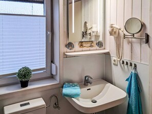 A bathroom with a sink, mirror, and hairdryer. There is a window with blinds and a potted plant on the windowsill. - Holiday Home in GrÃ¶mmitz (Groemitz)
