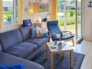 A modern living room with a grey sofa, a blue armchair, and a small table with a vase. - Holiday Home in GrÃ¶mmitz (Groemitz)