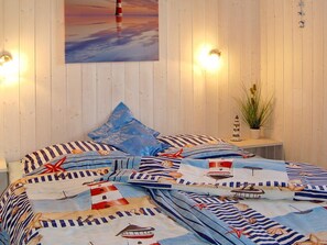 A bed with a nautical-themed bedspread, a blue pillow, and a wall-mounted painting of a sunset. - Holiday Home in GrÃ¶mmitz (Groemitz)