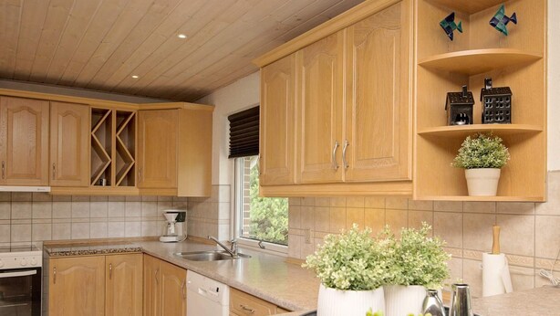A kitchen with wooden cabinets, a built-in oven, a coffee maker, and a window with blinds. - 9 Person Holiday Home in Blavand (Blavand)