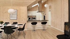 Moderni keittiö, jossa on puuseinät, valkoisella pöydällä ja mustilla tuoleilla varustettu ruokailutila sekä musta liesi.