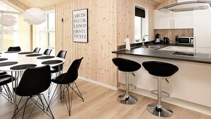 Moderni keittiö, jossa on puusisustus, ruokailutila pyöreällä pöydällä ja mustilla tuoleilla sekä keittiösaareke jakkaroineen.