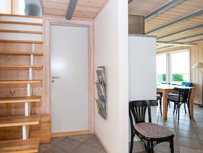 A room with a wooden staircase, a white door, a dining area with a table and chairs, and a window with a view.