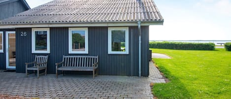Un bâtiment doté d’un toit recouvert de tuiles, d’une cheminée et d’un espace d’entrée pavé avec deux bancs.