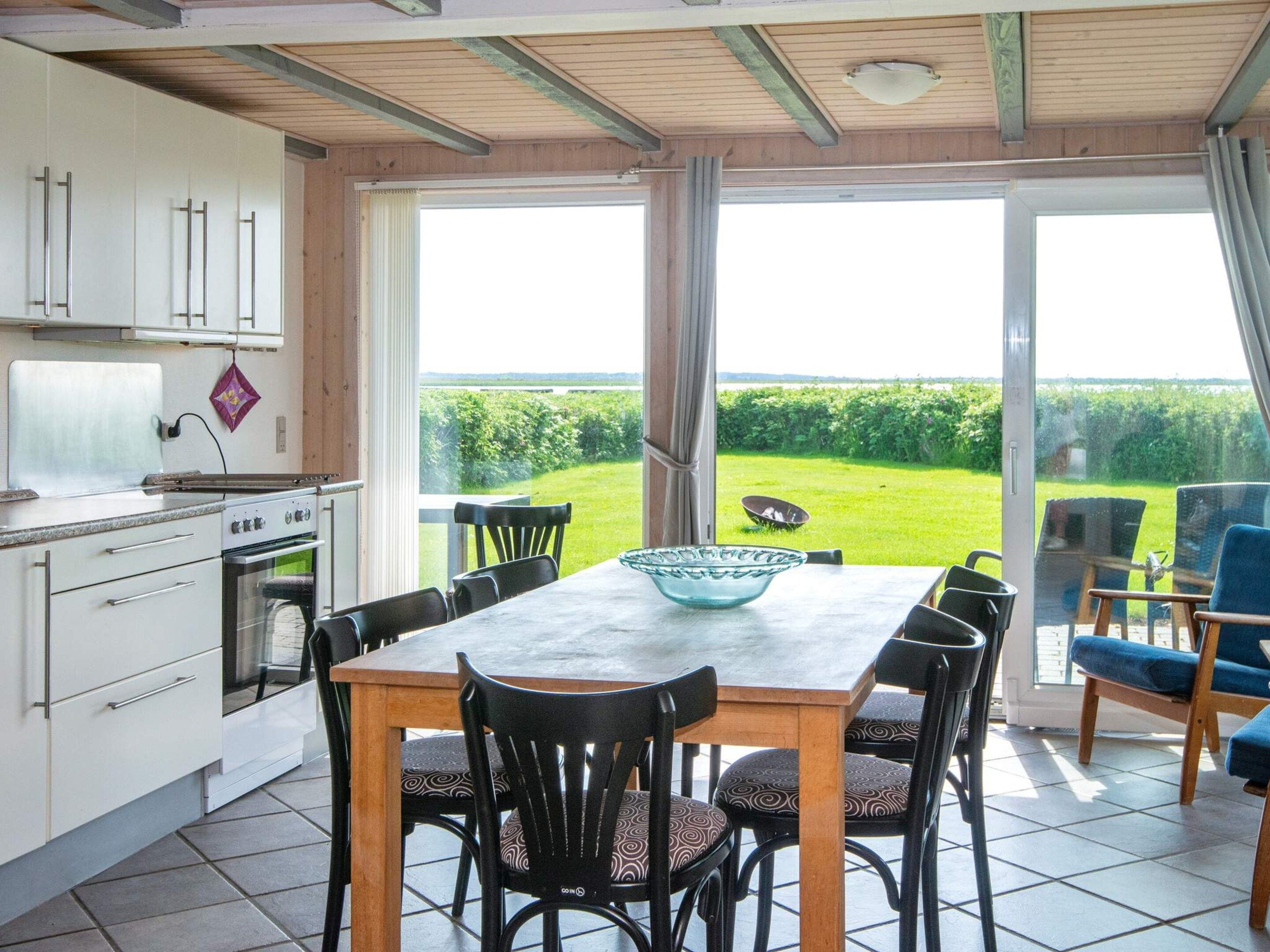 Une cuisine avec une grande table et des chaises, donnant sur un paysage verdoyant grâce à de grandes portes vitrées.