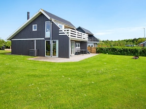 A modern house with a large deck, a covered patio, and a well-maintained lawn.