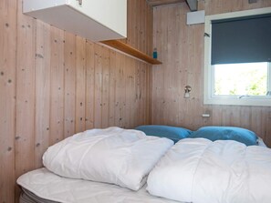 Un dormitorio con cama, paredes de madera, una ventana y un estante.