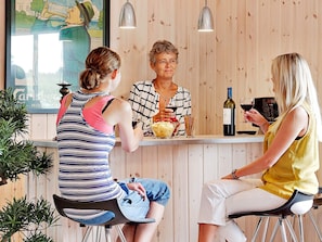 Three people seated at a wooden bar with a bottle of wine and a bowl of food. - Pet Friendly Holiday Home in Bogense with Hot Tub (Bogense)