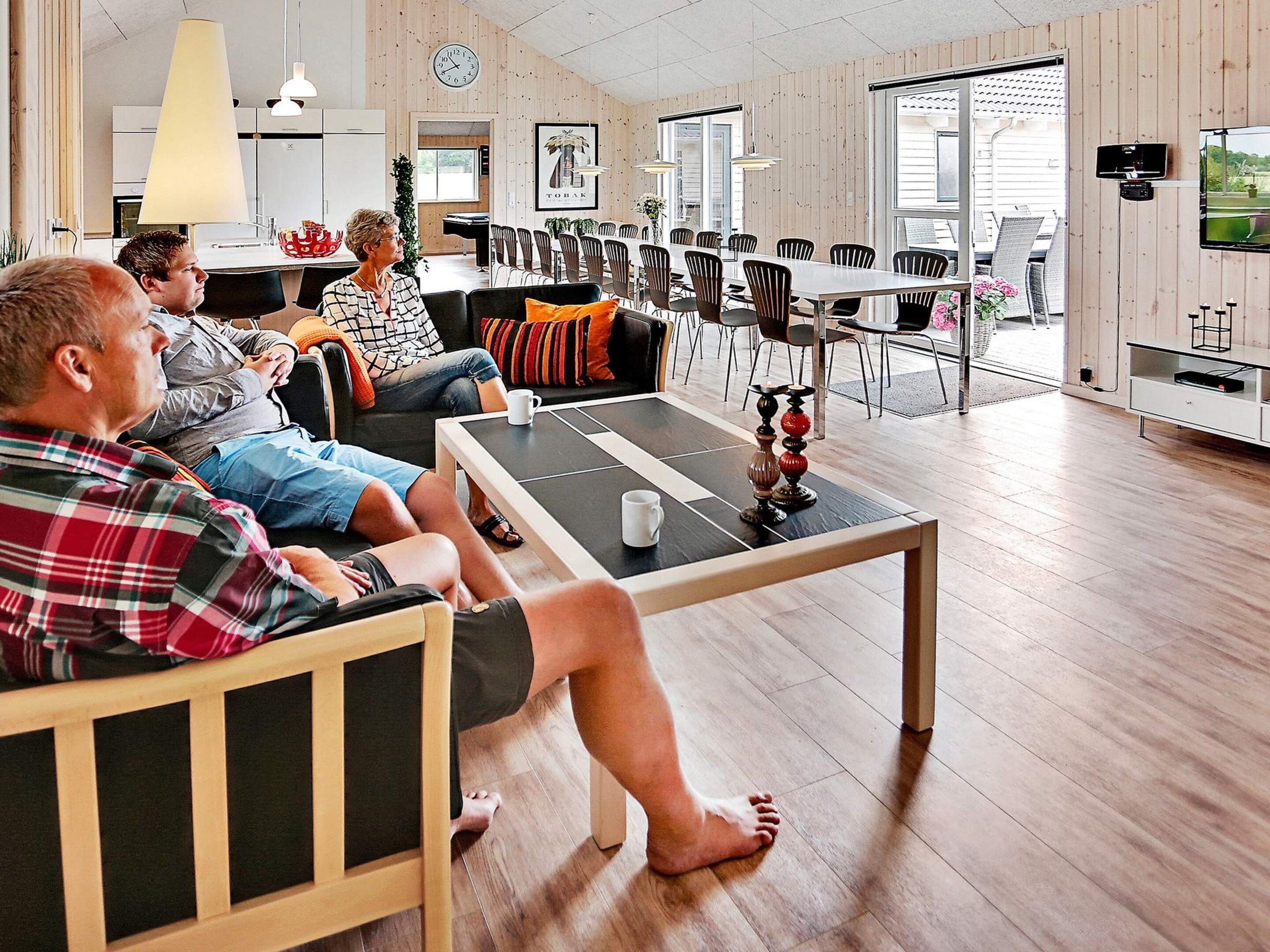 A spacious living area with a long table, comfortable seating, and a television mounted on the wall.