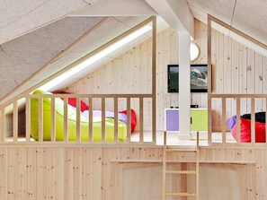 A loft bedroom with a wooden sloped ceiling, bunk beds, a TV, and a ladder.