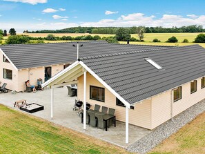 A two-story building with a sloped roof, outdoor seating area with tables and chairs, and a covered patio. - Pet Friendly Holiday Home in Bogense with Hot Tub (Bogense)