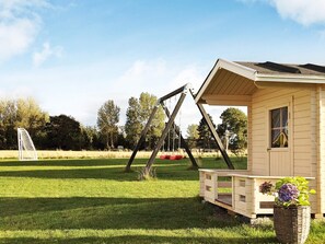 A wooden playhouse with a porch and a swing set in a grassy field.