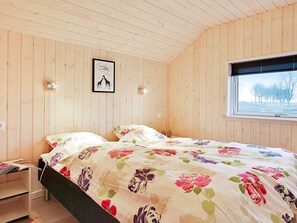 A bedroom with a bed, a nightstand, a framed picture, and a window with a view of trees.