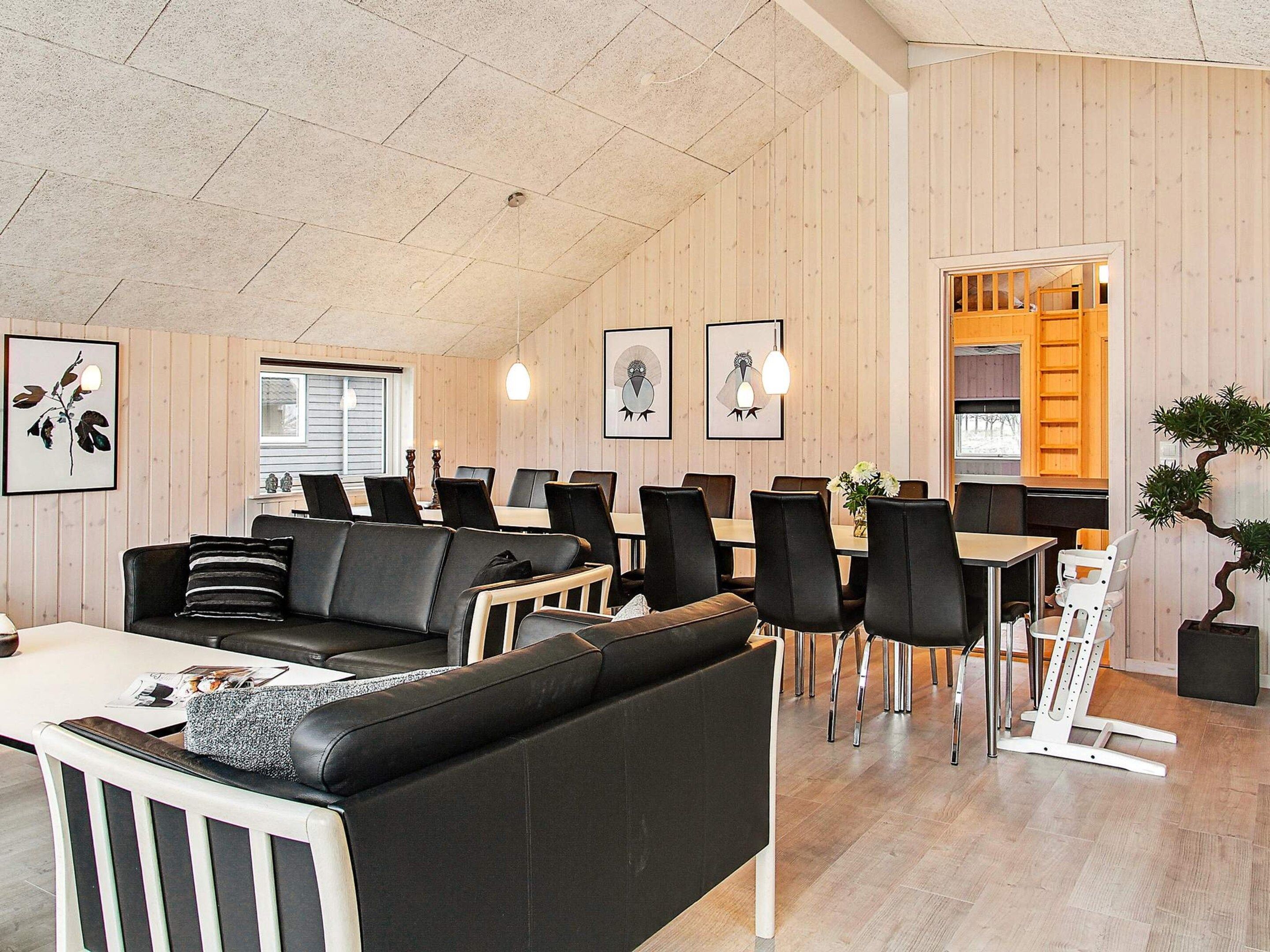 A modern interior with a black leather sofa, dining tables, and chairs, wooden walls, and framed artwork.