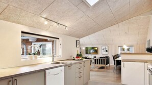 Eine moderne Küche mit Geschirrspüler, ein Essbereich mit grau-weißem Sofa und einem an der Wand montierten Fernseher.
