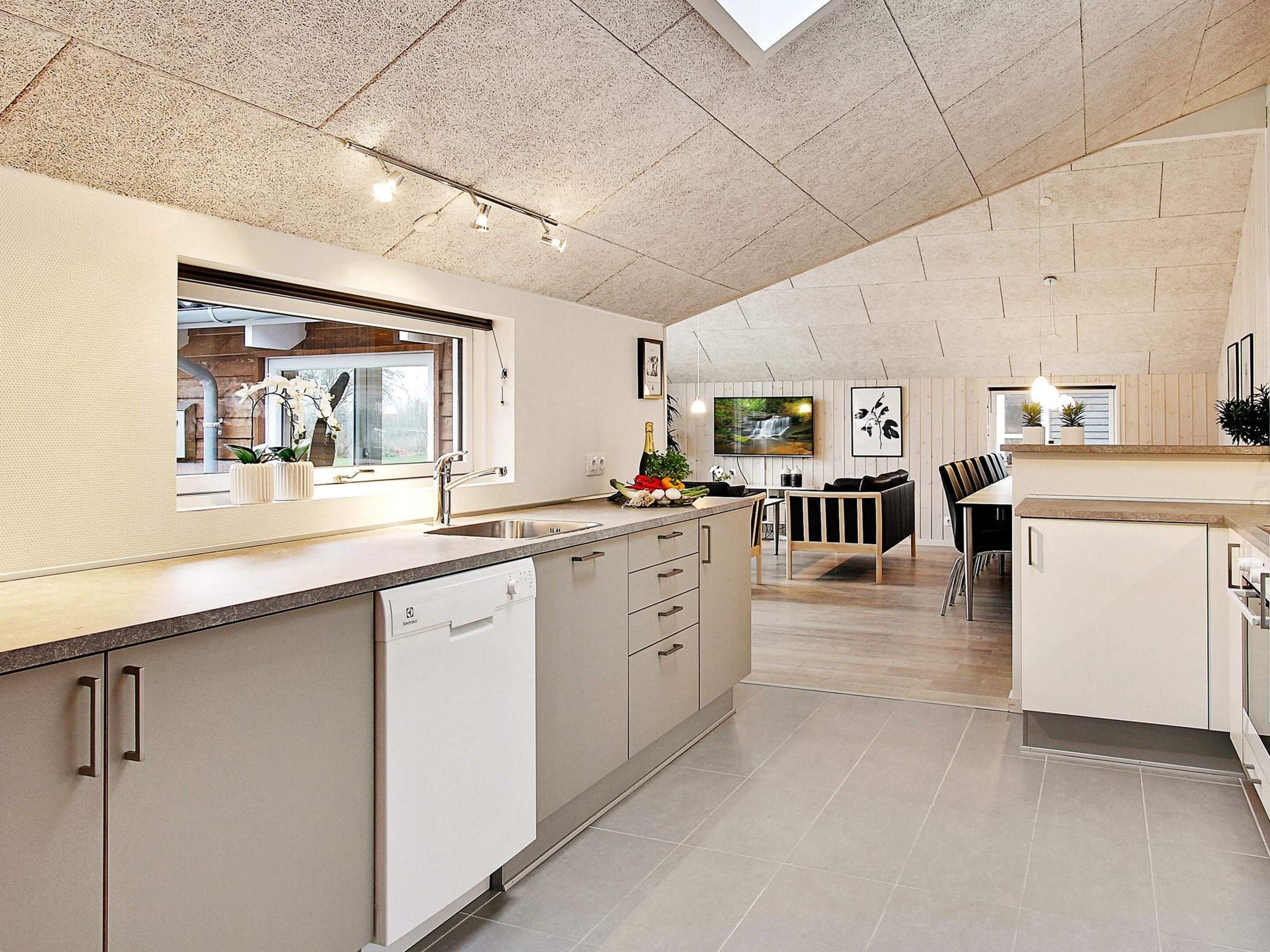A modern kitchen with a dishwasher, a dining area with a table and chairs, and a large window with a view of the outdoors.