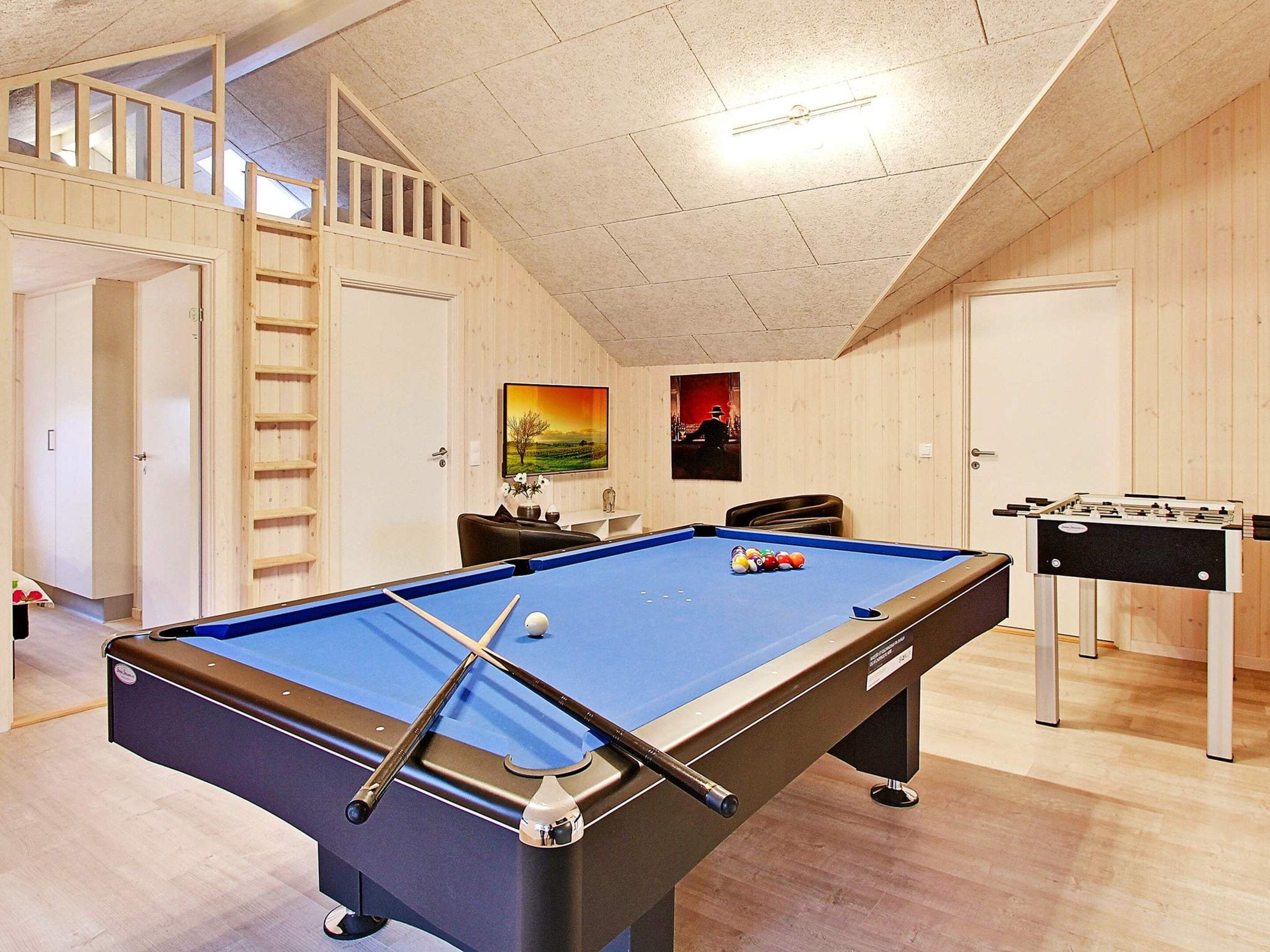 A pool table with a foosball table, wooden walls, and a staircase.