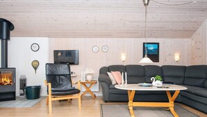 A cozy living room with a fireplace, a sofa, a chair, a TV, and a ceiling fan. - Classic Retreat in Bork Havn - By Traum Ferienwohnungen (Hemmet)