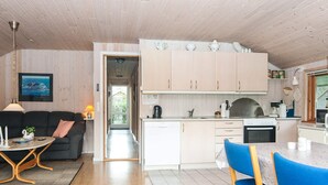 A modern kitchen with white cabinets, a dining area with blue chairs, and a living room with a dark sofa. - Classic Retreat in Bork Havn - By Traum Ferienwohnungen (Hemmet)