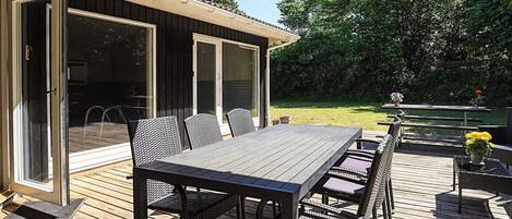 Terraza al aire libre con mesa y sillas, un espacio cubierto con una puerta y vista a un jardín con césped.