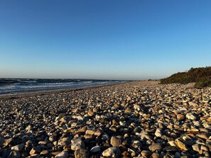 Una spiaggia rocciosa con onde, cielo sereno e una costa in lontananza.