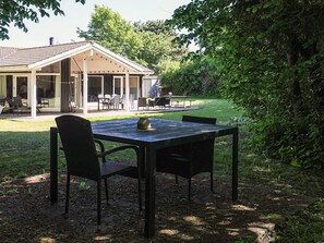 A covered patio with outdoor seating, a table with chairs, and a view of a house in the background. - 4 Star Holiday Home in Gilleleje (Gilleleje)