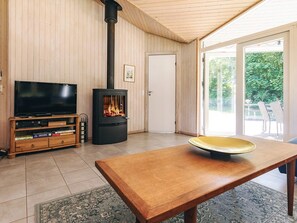 Un soggiorno con televisione, stufa a legna, tavolo da pranzo e vista sul panorama esterno.