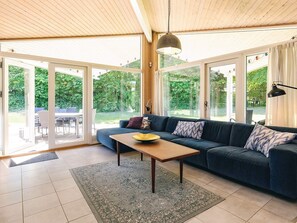 A modern living room with a sofa, a coffee table, and a dining area visible through glass doors. - 4 Star Holiday Home in Gilleleje (Gilleleje)