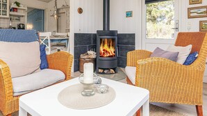 Ein gemütliches Wohnzimmer mit Korbmöbeln, einem weißen Tisch und einem Kamin mit brennendem Feuer.