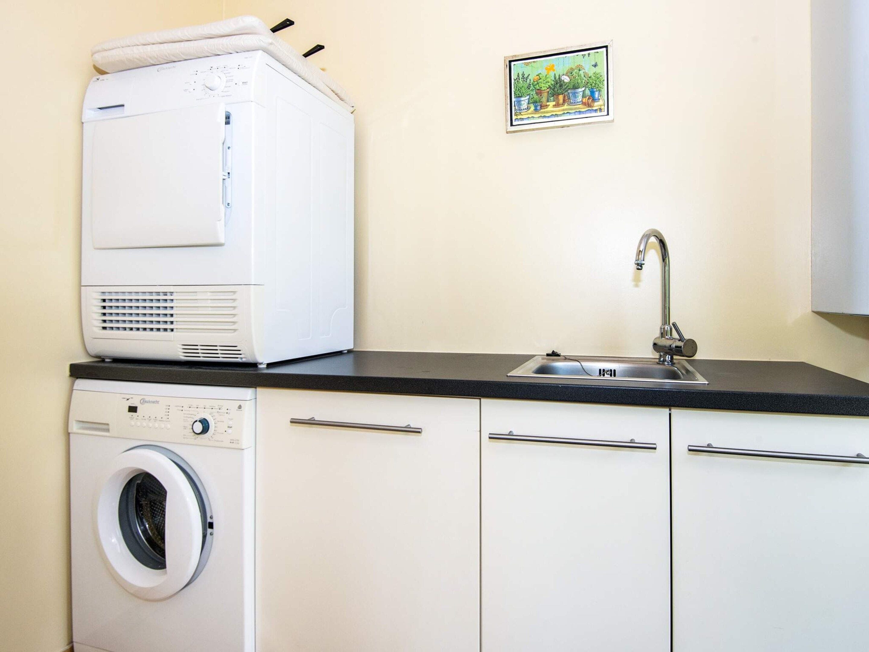 Une cuisine compacte équipée d’un lave-linge, d’un évier et d’un petit objet décoratif accroché au mur.