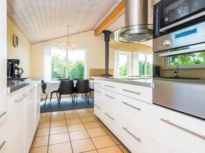 A modern kitchen with white cabinets, a stainless steel range, and a dining area with a table and chairs. - 5 Star Holiday Home in Hovborg (Hovborg)