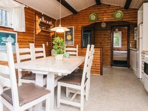 A wooden cabin interior with a dining table, chairs, a potted plant, and a kitchen area. - 4 Star Holiday Home in Blavand (Blavand)