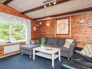 A cozy cabin interior with a sofa, a small table, and a window with a view of greenery. - 4 Star Holiday Home in Blavand (Blavand)
